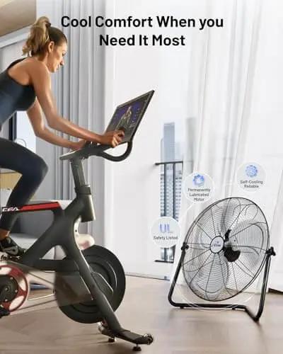 Cyclist using exercise bike near 20 Inch Heavy Duty Floor And Wall Mount Fan For Industrial Cooling With 5750 CFM High Velocity Three Speed And 360 Degree Tilt Head Black UL Listed For Garage Workshop Office And Home.