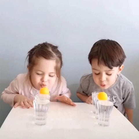Two children playing a game with 40mm colorful table tennis balls on glass cups, using 185 Pcs Colorful Table Tennis Balls for kids' fun activities.
