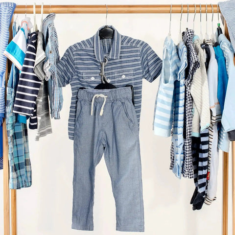 Children's striped shirt and gray pants on a wooden clothing rack with various kids' outfits in blue and white tones.