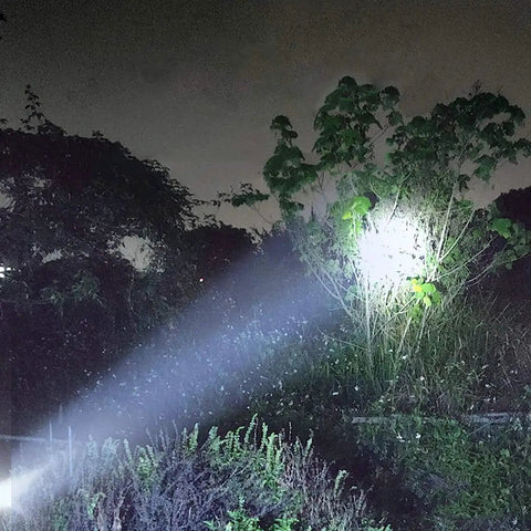 Solar Rechargeable Multi Function 1000 Lumens LED Flashlight With Emergency Strobe Light illuminating a tree at night outdoors