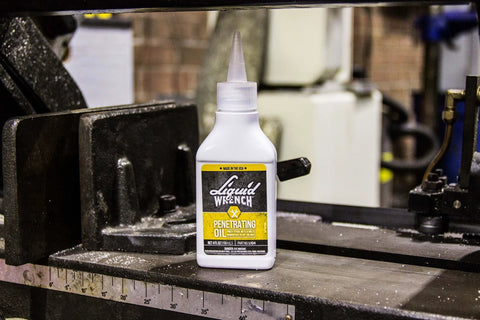 LIQUID WRENCH PENETRATING OIL 4 OZ DROPPER on a workshop table with machinery in the background.