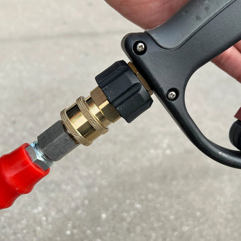 Close-up of brass M22 to 3/8 quick-connect pressure washer coupler on a black spray gun with red hose.