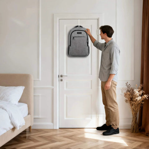 Person hanging a gray backpack on a white door in a modern bedroom with wooden floor and a beige bed.