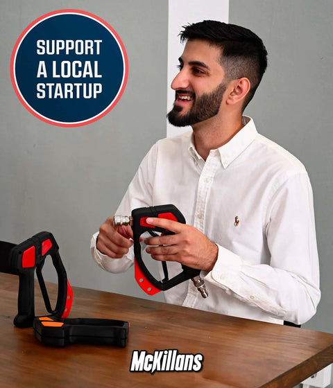 Man holding a pressure washer handle at a table, promotional sign "Support a Local Startup" in background, McKillans logo.