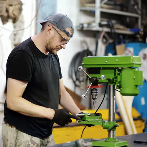 Worker using green industrial drill press in workshop.