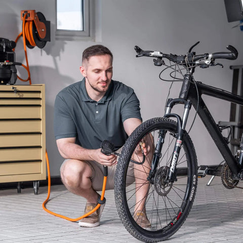 Man using Retractable Air Hose Reel With 180 Degree Swivel Bracket For Ceiling Or Wall Mount Three Eighths Inch By Fifty Foot Hybrid Hose on bicycle tire