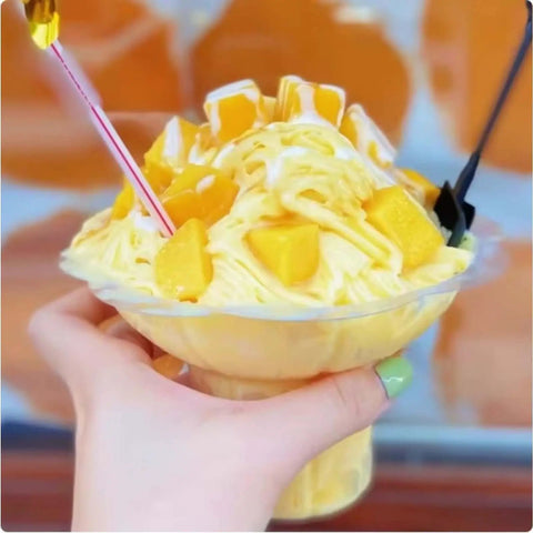 Mango snow ice dessert in clear disposable cup with two spoons