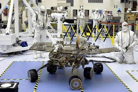 Engineers in cleanroom inspecting rover with protective suits and equipment
