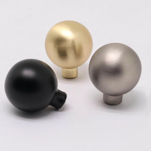 Three assorted cabinet knobs, including matte black, brass, and matte gray zinc alloy, each with a round ball design, ideal for drawers.
