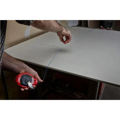 Milwaukee Chalk Line Reel Set F in use, showing a red reel with 100 ft blue line marking layout on a drywall surface.