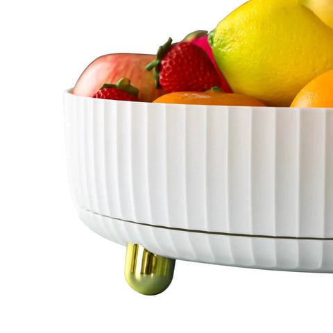 Decorative white ceramic fruit bowl with gold accents filled with assorted fruits.
