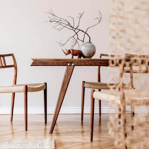 Mid-century modern dining area with wooden table, two chairs, and decorative branches in ceramic vase.