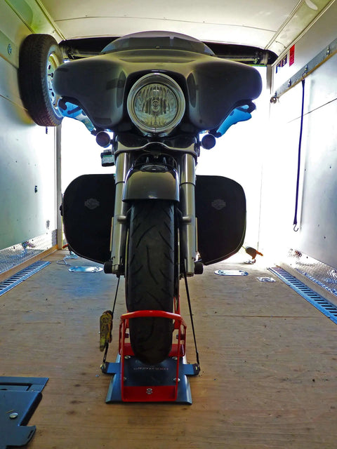 Front view of motorcycle secured in Deluxe One Size Fits All Orange And Black Motorcycle Wheel Chock With Quick Disconnect Mounting Plate And Built In Front Tire Tie Down Solid Powder Coated Steel Construction Self Locking Deluxe Wheel Chock For Easy Trailering From Lock N Load.