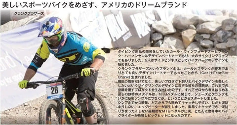 Mountain biker in action during a race wearing a colorful jersey and helmet, with a rocky terrain and banners in the background.