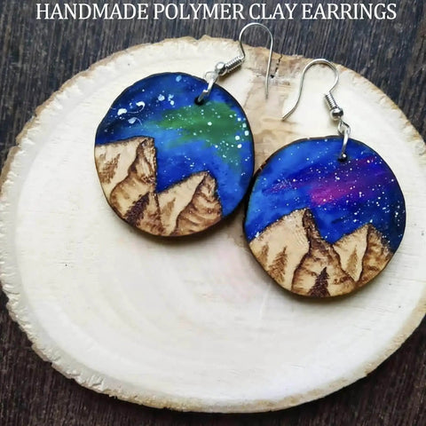 Handmade polymer clay earrings with mountain and night sky design displayed on wooden base