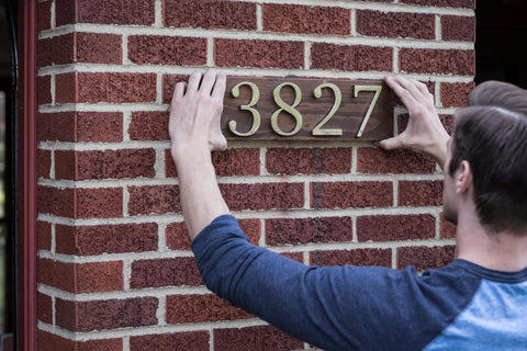 Man installing house number plaque using Heavy Duty Clear Double Sided Mounting Tape For All Weather Indoor And Outdoor Use 1 Inch By 60 Inch Roll Transparent Adhesive That Holds Up To 30 Pounds Per Roll Ideal For Metal Glass Wood Concrete Brick Tile Ceramics And More.