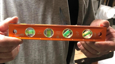 Person holding Savage 9 Inch Magnetic Torpedo Level With Four Neodymium Magnets And Four Vials For 30 Degree Conduit Bends Built From Solid Aluminum For Lifetime Durability Bright Orange Finish For Easy Visibility On Any Job Site.