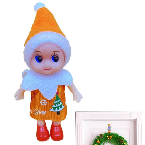 Christmas elf doll with orange hat and festive dress, standing next to door with holiday wreath.