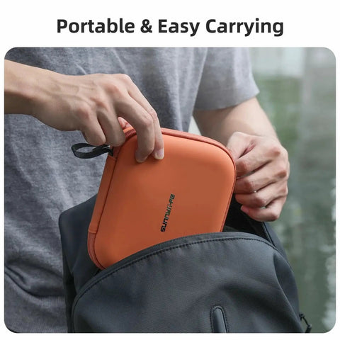 Person placing an orange portable carrying case into a backpack, showcasing compact storage for easy travel and protection of contents.