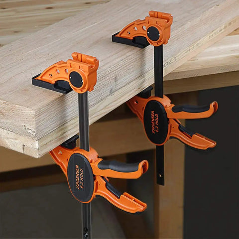 Two Pack Six Inch One Hand Clamp and Spreader Set with 300 lb clamping force attached to a wooden table, orange and black