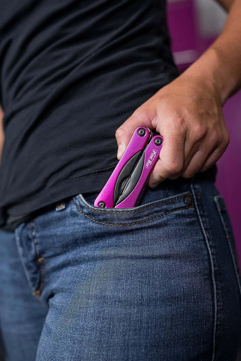 Person placing Pink 14-In-1 Aluminum Multi-Tool With Stainless Steel Tools into jeans pocket, illustrating compact size for everyday carry.