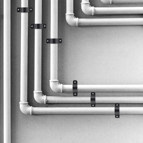 1/2 inch pipe support clamps, black metal, securing white PEX/Copper/CPVC pipes to wall
