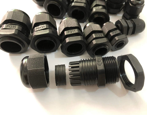 Assorted black plastic cable glands with threaded connectors and labels, arranged on a white surface.