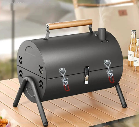 Black portable charcoal grill with wooden handle on a wooden table, features two latches and chimney, designed for outdoor cooking.