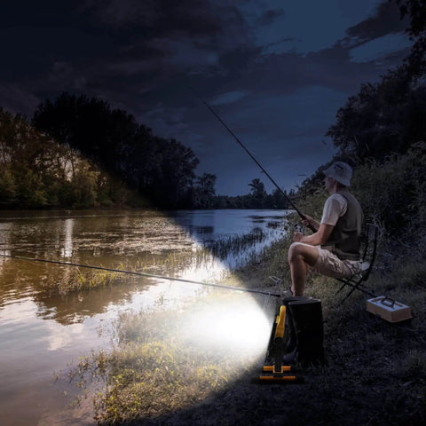 Rechargeable 100W LED Work Light illuminating a nighttime fishing scene by a lake, showing its Beast Mode Brightness and stand.