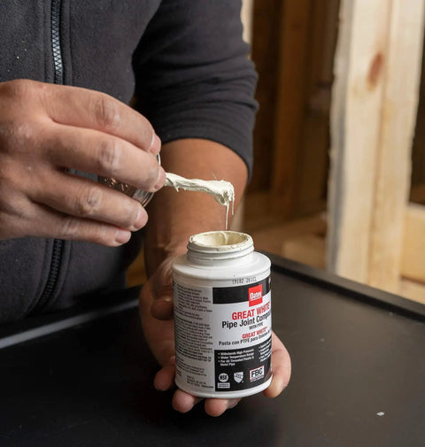 Person holding Pro Grade Pipe Joint Compound with PTFE brush, 8 oz, white non-hardening paste for threaded joints, Oatey 31231