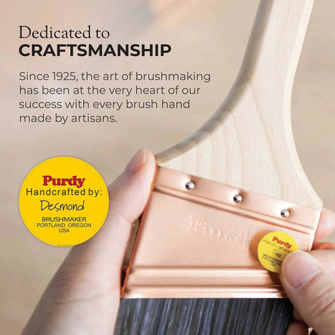 Hand holding Purdy paintbrush with wooden handle and copper ferrule, showcasing craftsmanship dedication badge.