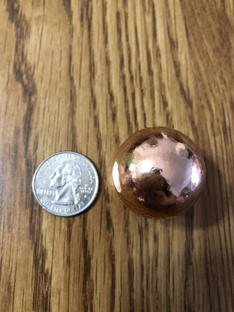 Unique Metals Pure Copper Sphere 1-1/8" next to a quarter for size comparison, on a wood surface; used for healing and decorative purposes.