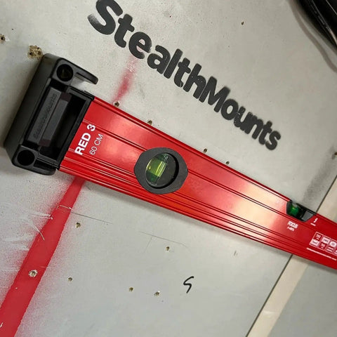 Yellow Universal Level Holder With Locking Mounts For All Levels In A 2 Pack Fits All Brands And Surfaces Ready For Secure Level Storage And Hassle Free Transport StealthMounts Built For Everyday Use No Brainer Setup holding a red level tool on a wall.