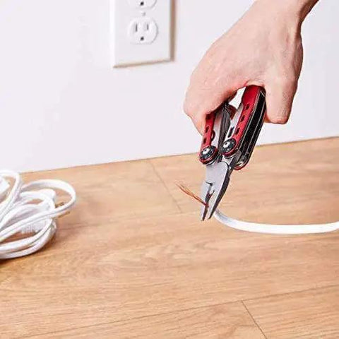 Using 10-In-1 Stainless Steel Multitool With Safety Lock And Red Nylon Sheath to cut wire on wooden floor