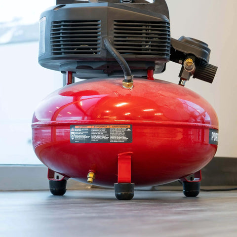 Red portable air compressor on wooden floor with metal tank and black motor, featuring vibration isolation rubber feet.