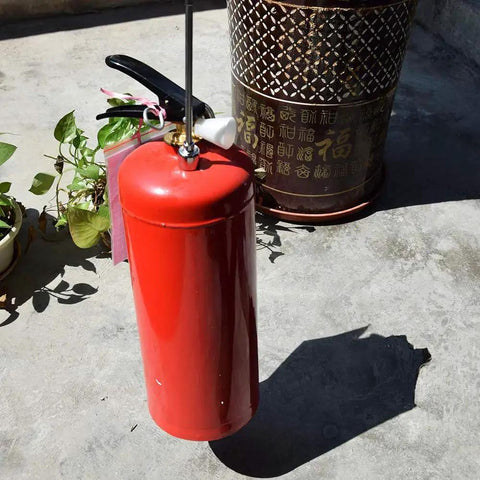 A red metal fire extinguisher with a black handle, placed on a concrete surface near decorative planters.
