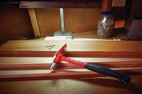 20 oz steel general purpose hammer with an ergonomic vibration-reducing grip, smooth face on a workbench next to nails and wood planks