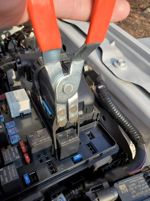 Automotive Relay Tester With Puller For 12V Cars And Trucks in use, showing relay removal with pliers inside a car's fuse box.