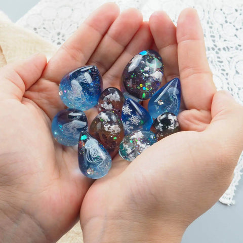 Hands holding colorful resin pendants made with Mini Egg And Waterdrop Silicone Molds Set Six Pieces Clear Resin Molds for DIY crafts