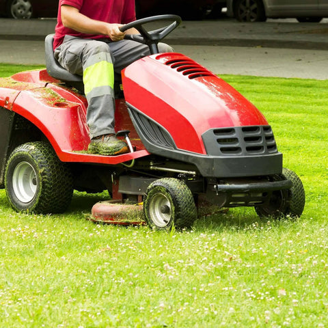 Riding lawn mower on grass being operated, side view, showing red body and steering details, outdoors.