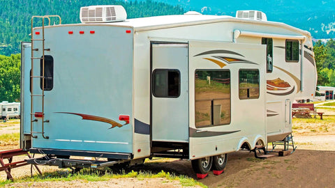 RV Leveling Blocks Kit for Dual Axle Travel Trailer With Ramp Chocks Rubber Mats Bubble Level and Carry Bag Heavy Duty HDPE Non Slip System Adjustable From One Half Inch To Four Inches In Minutes By OULEME installed under dual axle travel trailer in a campsite.