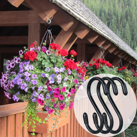 Colorful hanging flower baskets on a wooden porch with black metal S-hooks used for support, forest background visible.