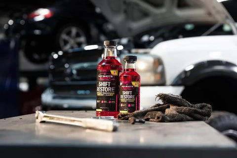 Shift Restore Automatic Transmission Additive 16 Oz Bottle for smoother shifts on a garage workbench with tools and cars