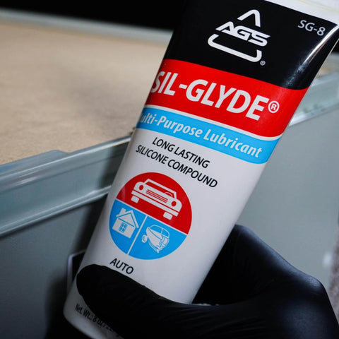 Close-up of SIL-Glyde Multi-Purpose All-Weather Lubricating Compound for All Surfaces - 8 oz Tube being held by gloved hand.