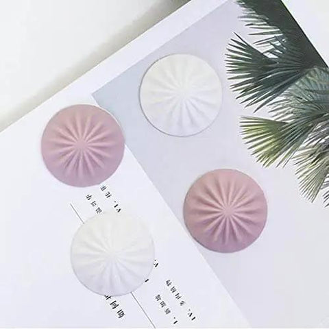 Soft silicone door stopper and wall protector cushions door impacts, reduces noise, in white and pink, placed on a book page.