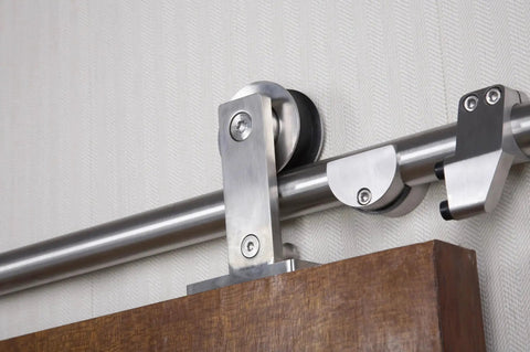 Close-up of Seventy Eight And Three Quarters Inch Single Roller Round Rod Barn Door Hardware Kit in champagne brass finish with wooden door.