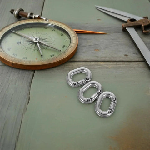 Three 8mm stainless steel marine-grade quick links on a green wooden surface with a compass and tools