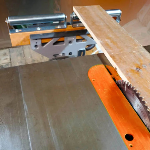 Wooden board on a table saw with stainless steel roller bracket set in the background.