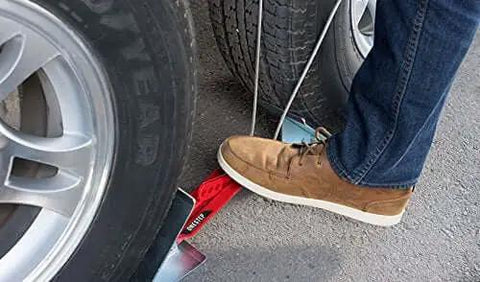 Using a foot to set the OneStep Wheel Chock Double Pack For Tandem Axle Trailers And RVs, 16 to 24 inch long, showing no kneeling setup.