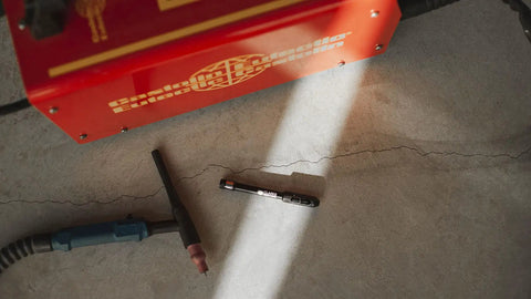 Professional TIG Welding Pen Holder With Metal Storage Case on workshop floor next to welding machine and torch, concrete backdrop